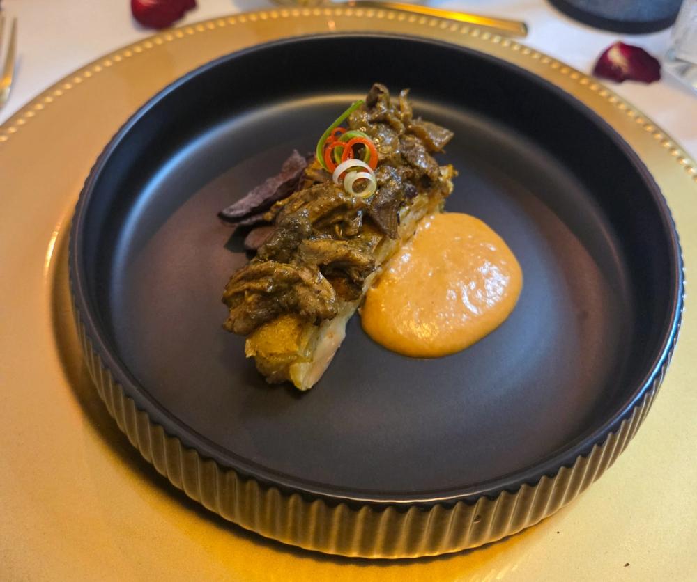 Signature Tarragon Curry Goat by Chef Kimberly Kee of Saucy Kim K, featuring slow-braised goat, vibrant sweet potato espuma, and technical garnishes on a luxury black ribbed plate. High-end Caribbean fusion private dining and bespoke catering serving estates in Newport RI, Greenwich CT, and Boston MA