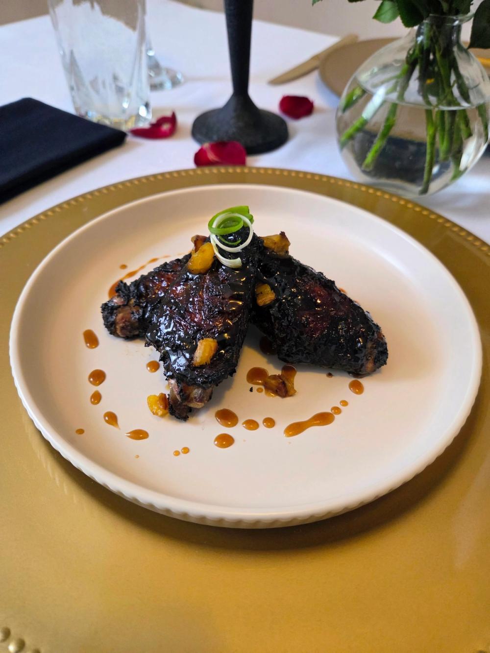 Artisan Jerk Chicken Wings by Chef Kimberly Kee of Saucy Kim K, featuring a signature pineapple rum reduction glaze and scallion garnish on a luxury gold charger. Premium Caribbean fusion catering and private dining services serving Rhode Island, Massachusetts, and Connecticut.