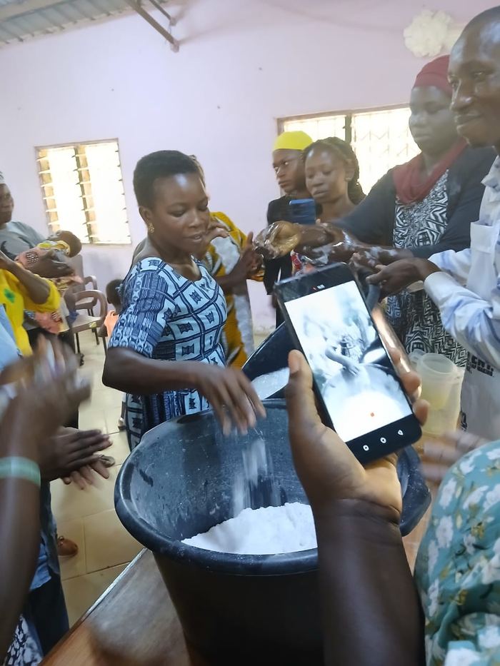 Women making soap indoors while another records the method