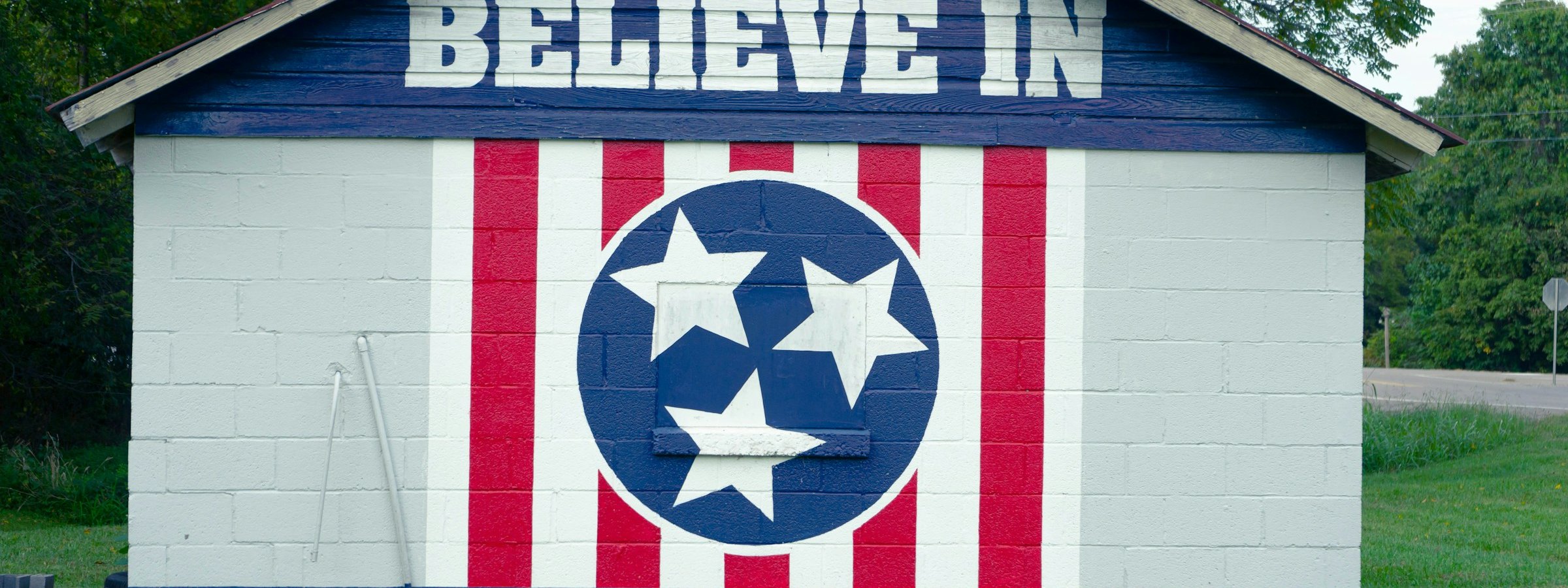 A mural reading 'I Believe in Clarksville' painted on a small shed with the Tennessee tri-star flag design.
