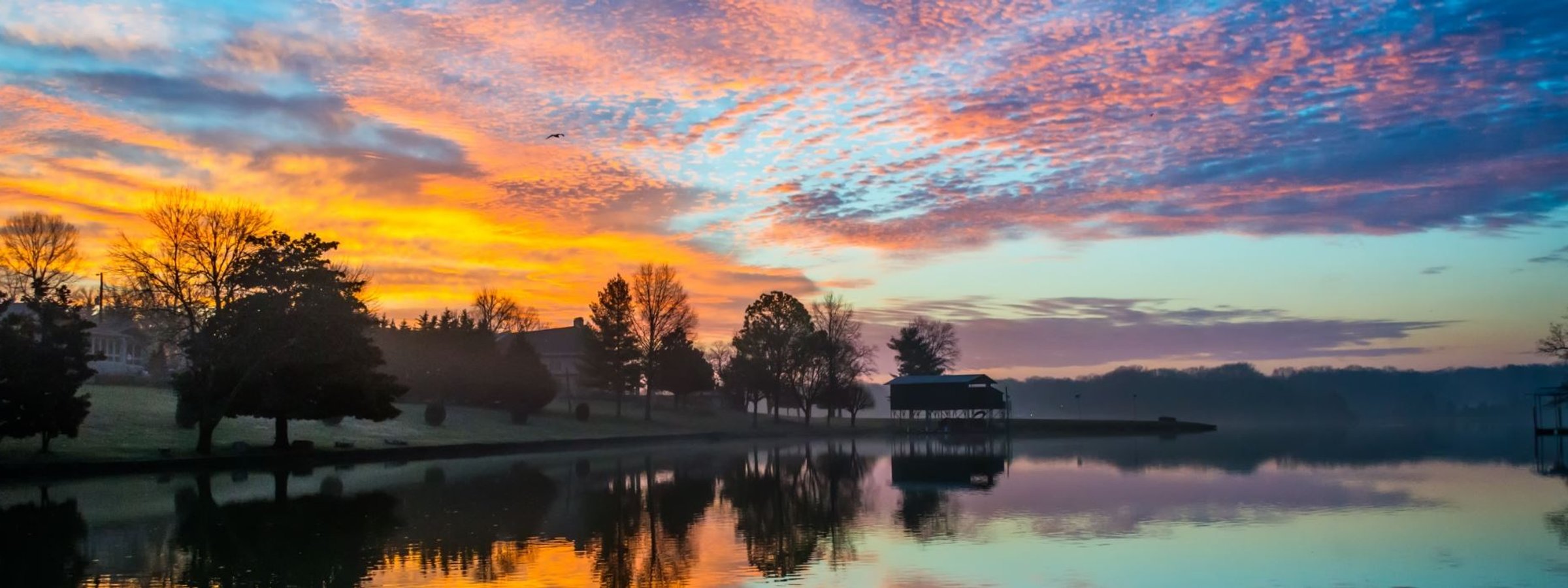 Sunrise over a Hendersonville lake, pink and orange clouds reflecting in still water.