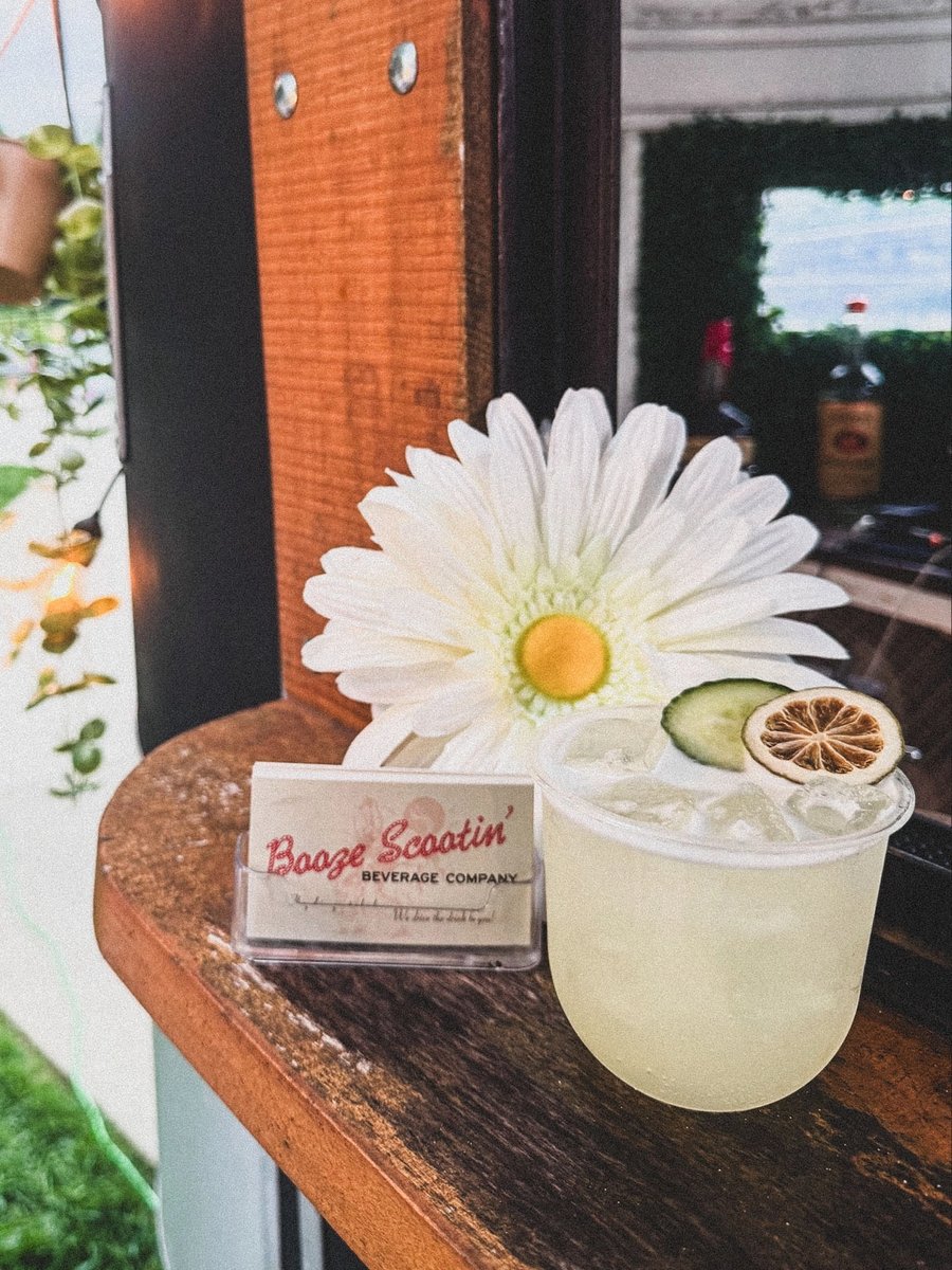 A cucumber-lime cocktail on the trailer's bar shelf next to a white daisy and a Booze Scootin' business card.