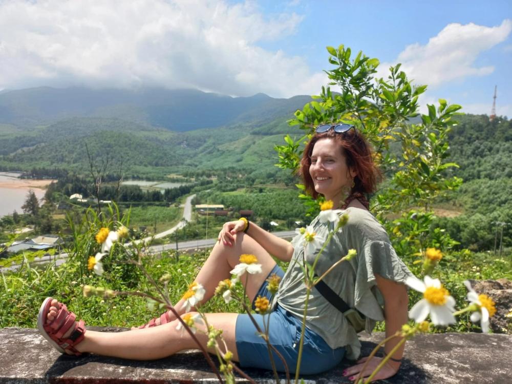 A Anica sentada numa encosta com malmequeres, a rir