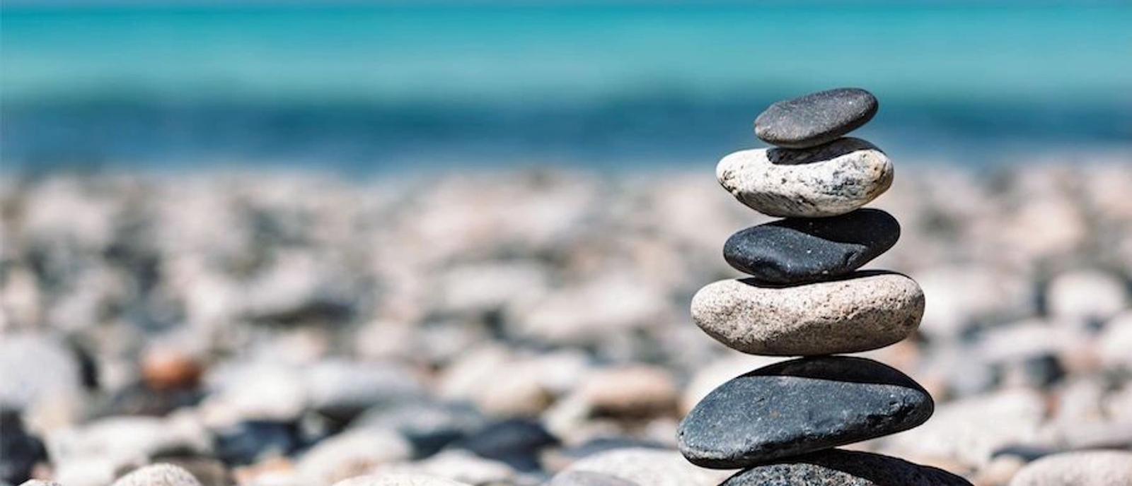 Stacked stones balanced on a beach with ocean waves and sand in the background, symbolizing strategic balance in business growth.