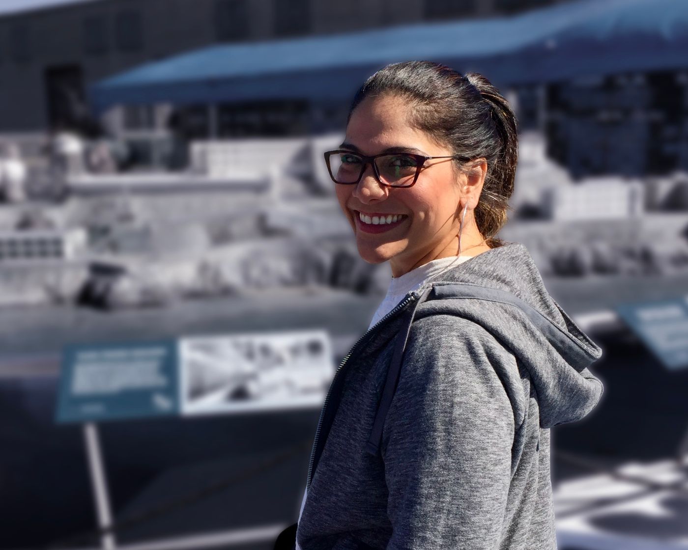 Kathia smiling at the camera on a sunny rooftop with a cityscape and blue tent visible in the background.