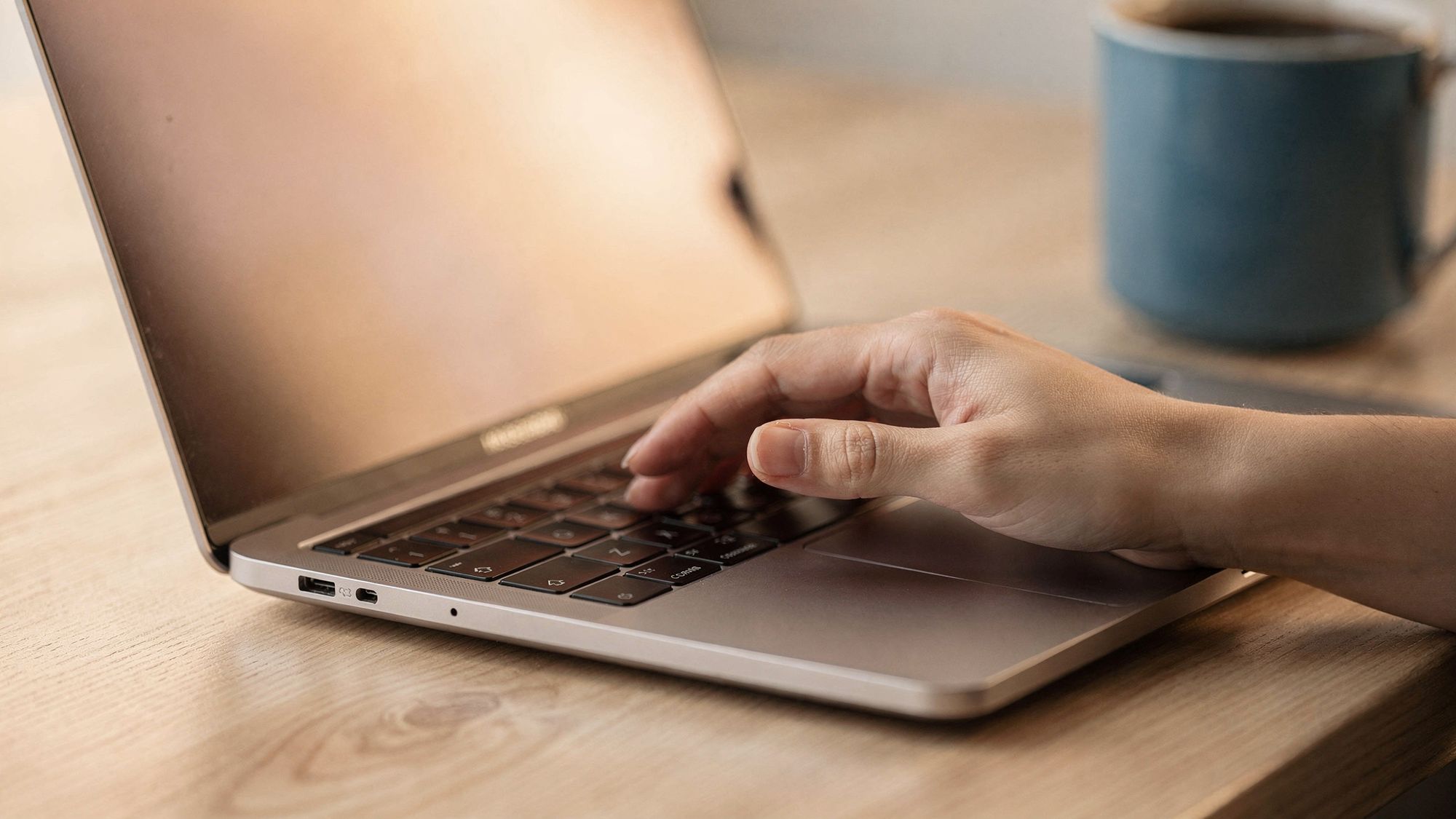 A close view of a hand resting on a laptop trackpad with the index finger lifted, lit by the warm glow of the screen.