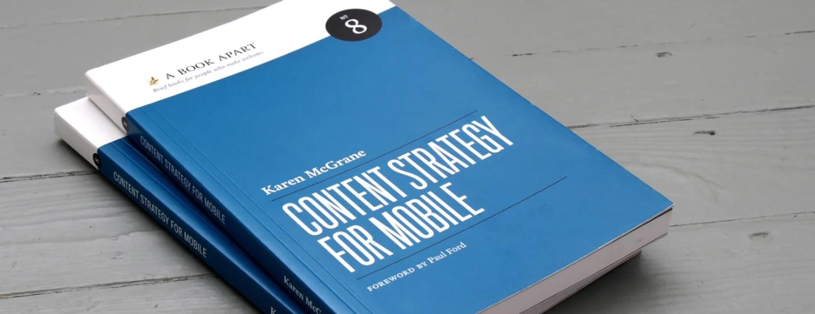Stacked books on a whitewashed wooden surface, with Karen McGrane's Content Strategy for Mobile guide prominently displayed.