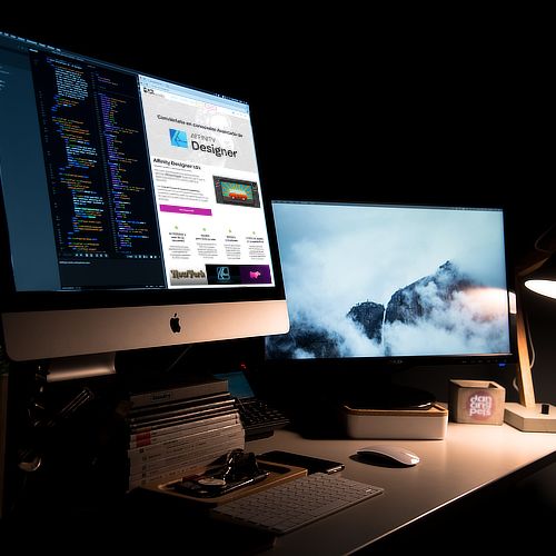 Designer's desk with dual monitors displaying website code and a custom web design interface for a service business.