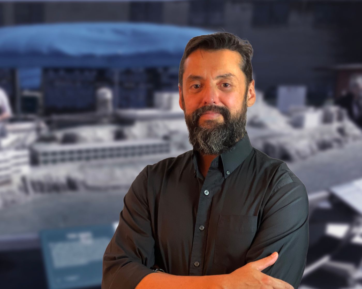 Julio wearing a dark button-up shirt, posed with arms crossed against an urban rooftop backdrop, representing Dancing Pels leadership.