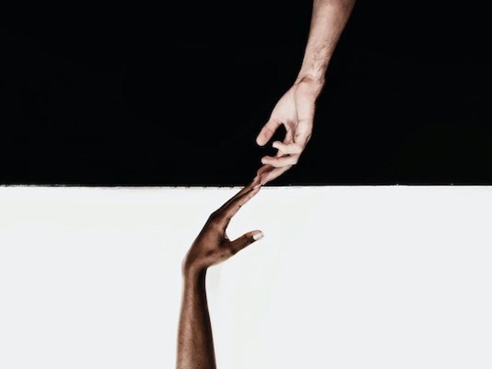 Two hands reaching toward each other in a gesture of connection and collaboration against a split black and white background.
