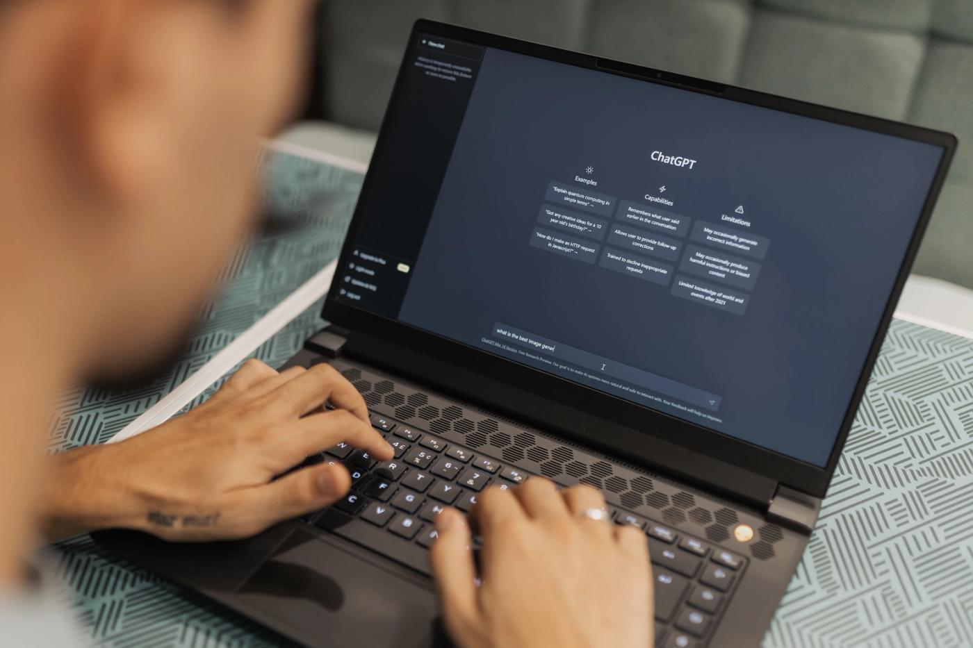 A person types on a laptop with the ChatGPT interface open on screen