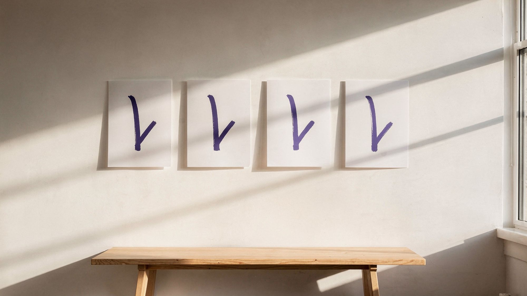 Four identical printed posters hang in an evenly spaced row along a warm white wall above a light wood bench, each showing the same violet brushstroke mark.