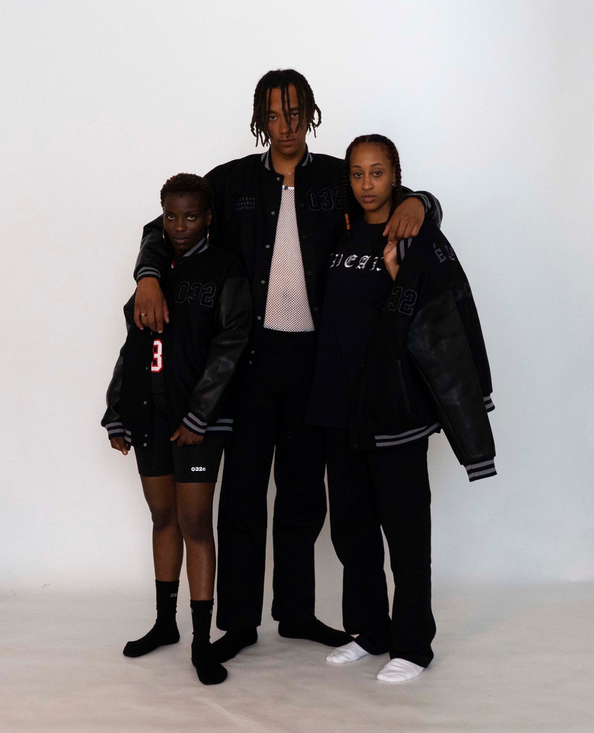 Mariama, Buyegi and Libell wear the 032c LoveSexDreams "Team Société" Varsity Jacket. Mariama pairs it with the neoprene shorts in black and the "Team Société" Football Jersey in Black. Buyegi and Libell both wear the straight leg trouser. Libell opts for the "Ideal" T-shirt, while Buyegi finishes his look with the Net tank in white