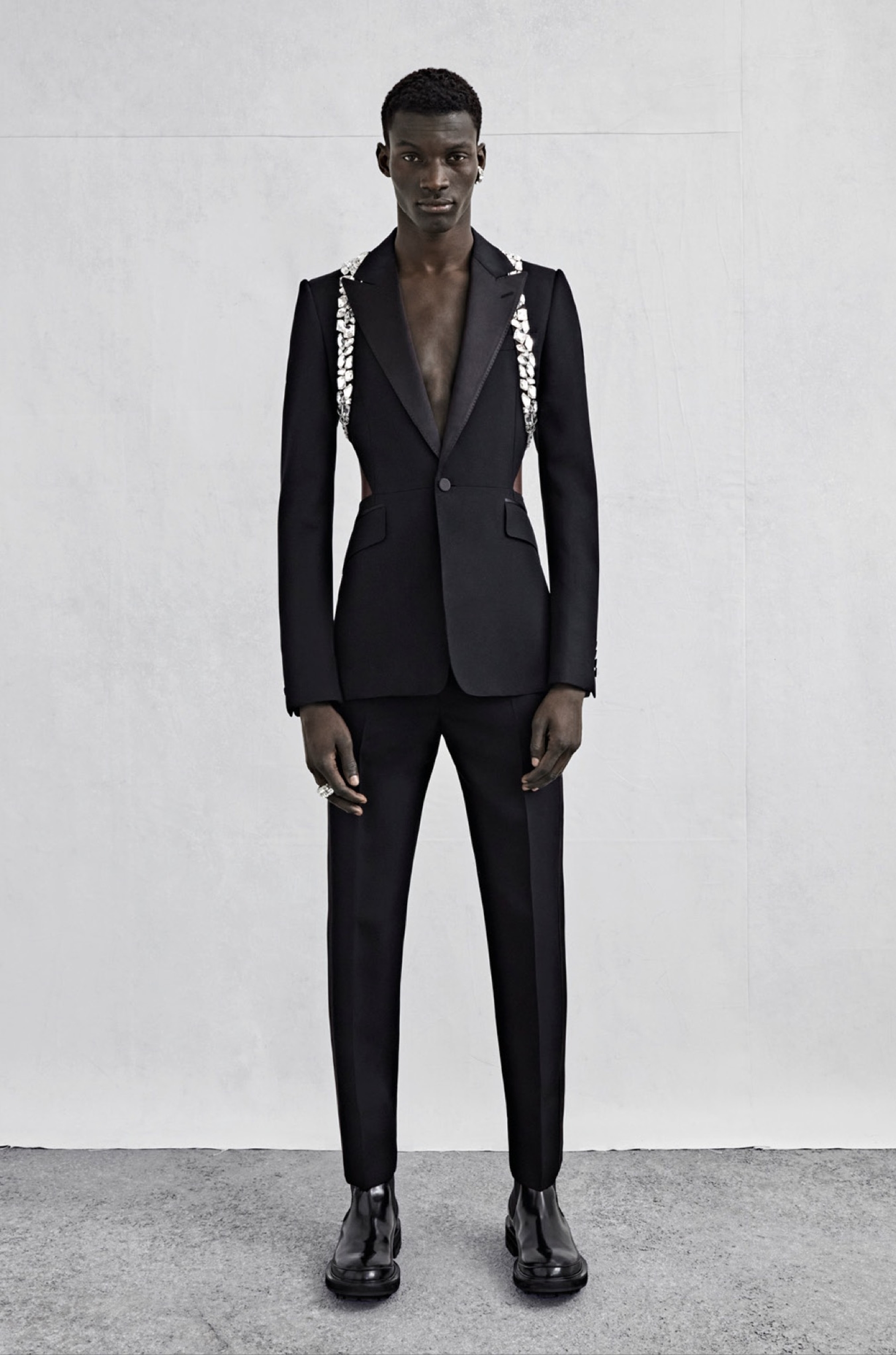A tailored jacket with a cutaway waist and back, tonal satin lapels and crystal harness embroidery in black barathea and cigarette trousers in black barathea with a tonal satin side stripe.