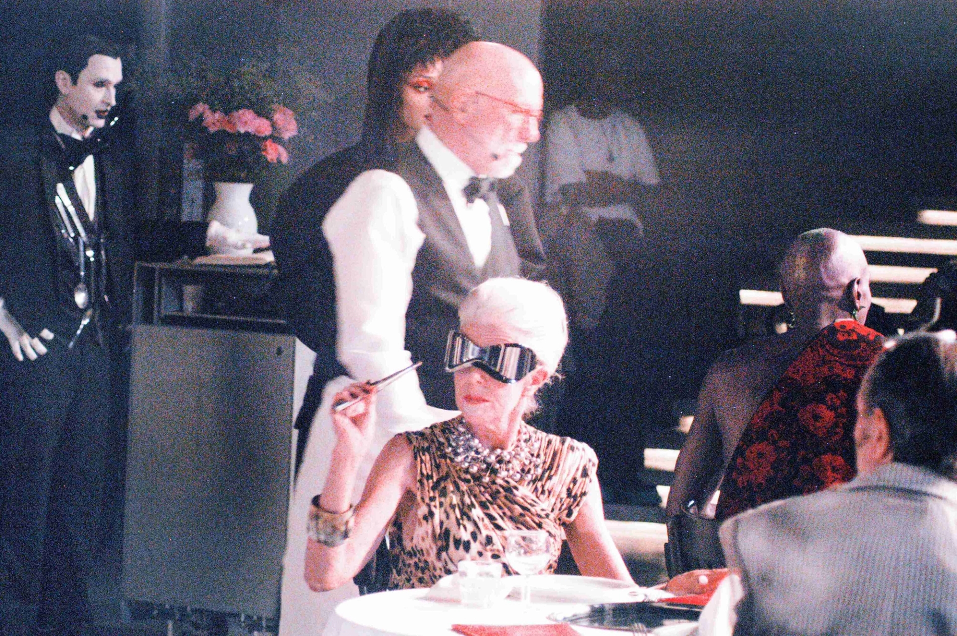 Agnes (center), glasses VINTAGE STYLIST'S OWN, dress VINTAGE ICEBERG from THE PARISIAN VINTAGE, necklace PANCONESI, bracelets ISABELLE TOLEDANO, rings MODEL'S OWN. George (waitor) shirt VINTAGE from COME ON EILEEN, bowtie CHARVET, vest DEADSTOCK, pants MODEL'S OWN. Andre (right) sash and pants DENZIL PATRICK from PUBLIC IMAGE, earrings and rings LARUICCI from AUTREMENT PR. Sofie (back), coat GUCCI, gown PRESSIAT, necklace Y/PROJECT.