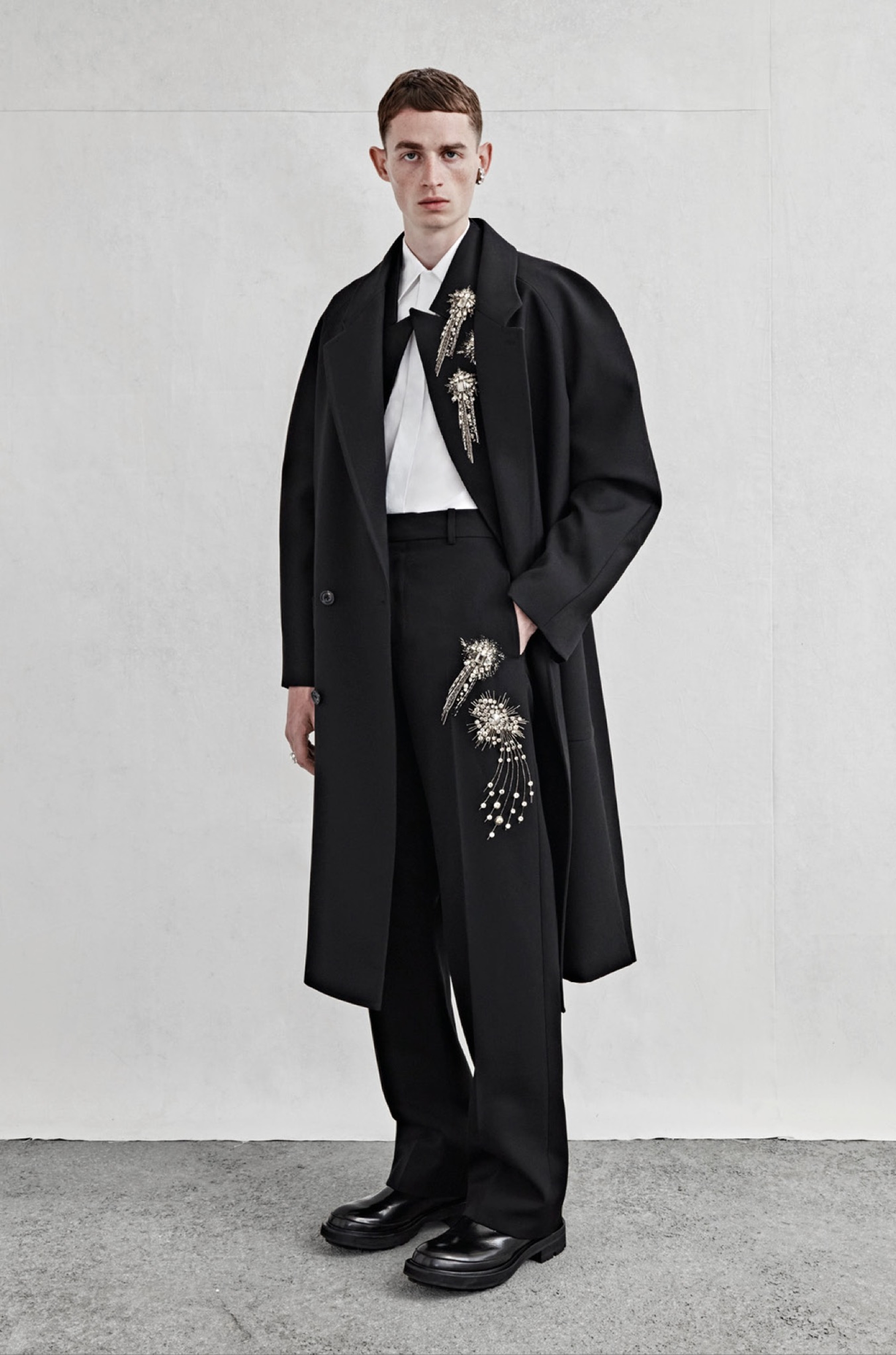 An oversized double-breasted tailored coat in black wool twill, a tailored waistcoat in black barathea with silver sequin and crystal astral embroidery, a shirt in white cotton poplin and tailored wide-legged trousers in black barathea with silver sequin and crystal astral embroidery.