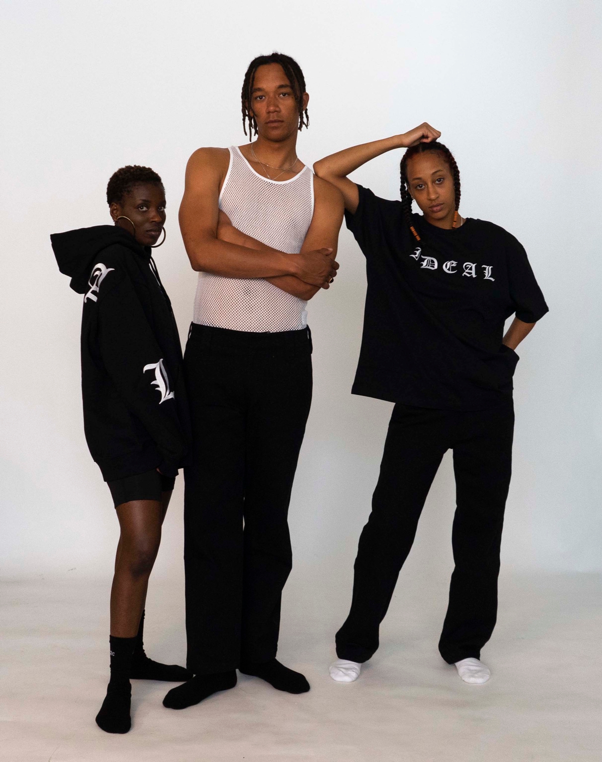 Mariama wears the 032c LoveSexDreams "Team Société"/"IDEAL" Hoodie in black, with neoprene shorts in black. Buyegi wears the Net Tank in white with straight leg trousers. Libell wears the "Ideal" t-shirt with straight leg trousers