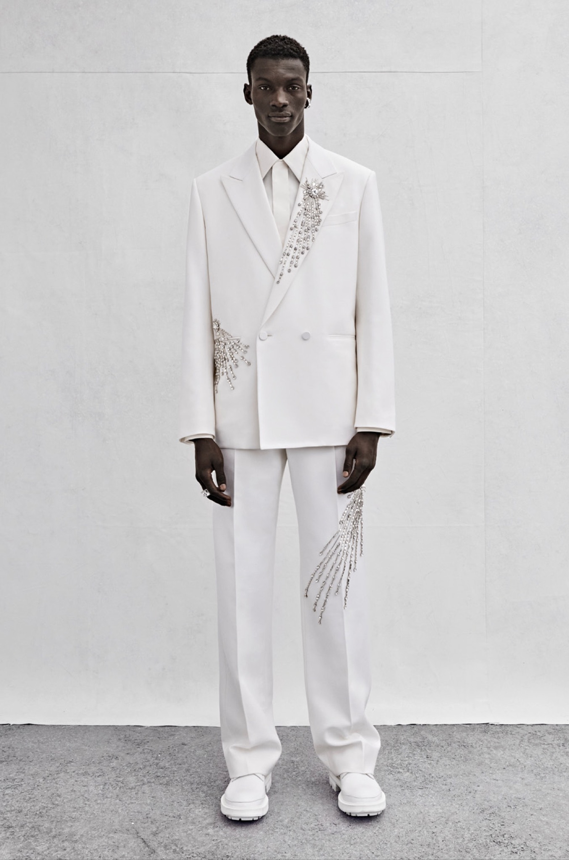 An oversized double-breasted tailored jacket in white wool twill with silver sequin and crystal astral embroidery, a shirt in ivory silk poplin and wide-legged trousers in white wool twill with silver sequin and crystal astral embroidery.