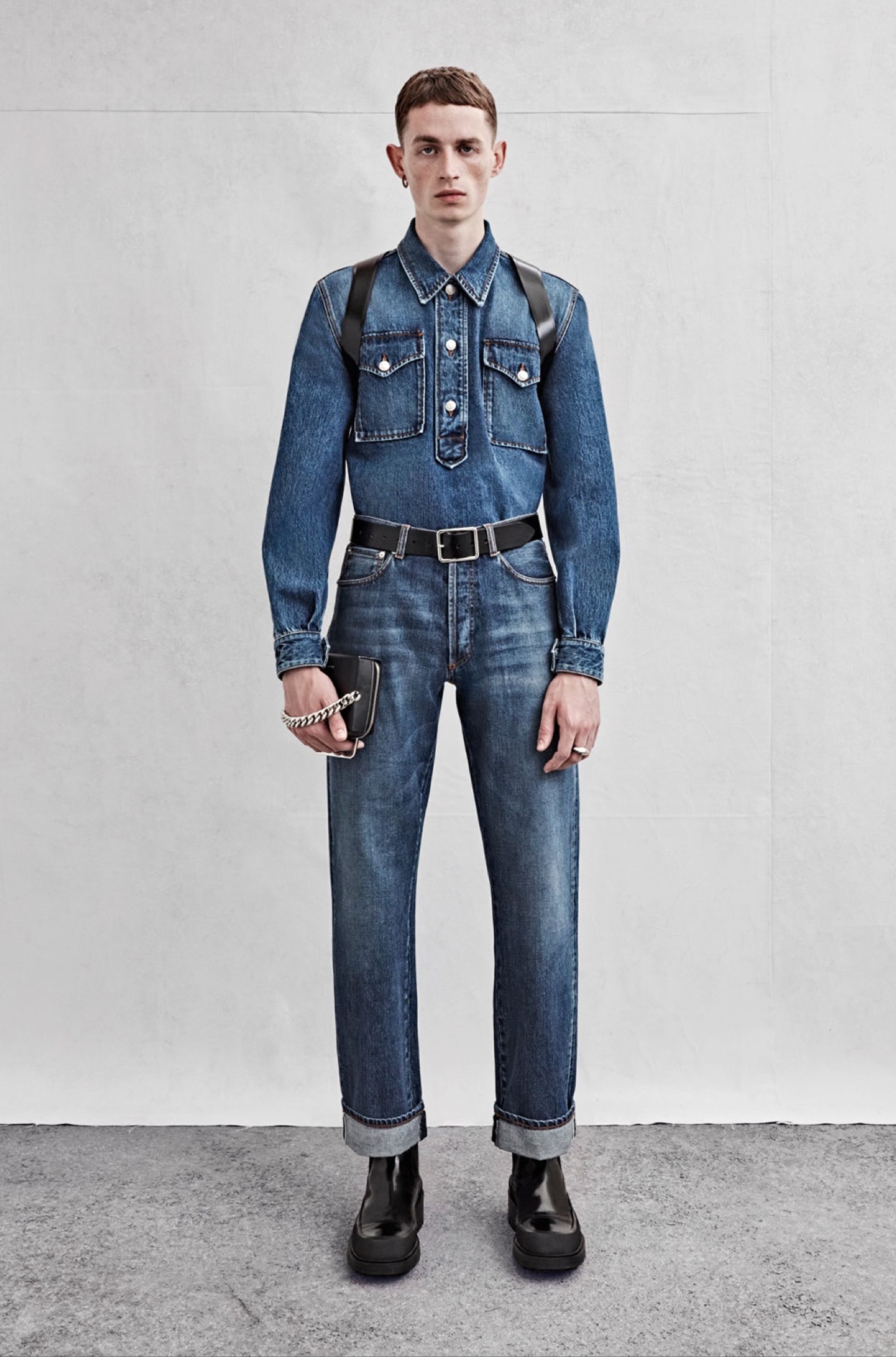 A pullover shirt in blue denim, a harness in black leather and jeans in blue denim.