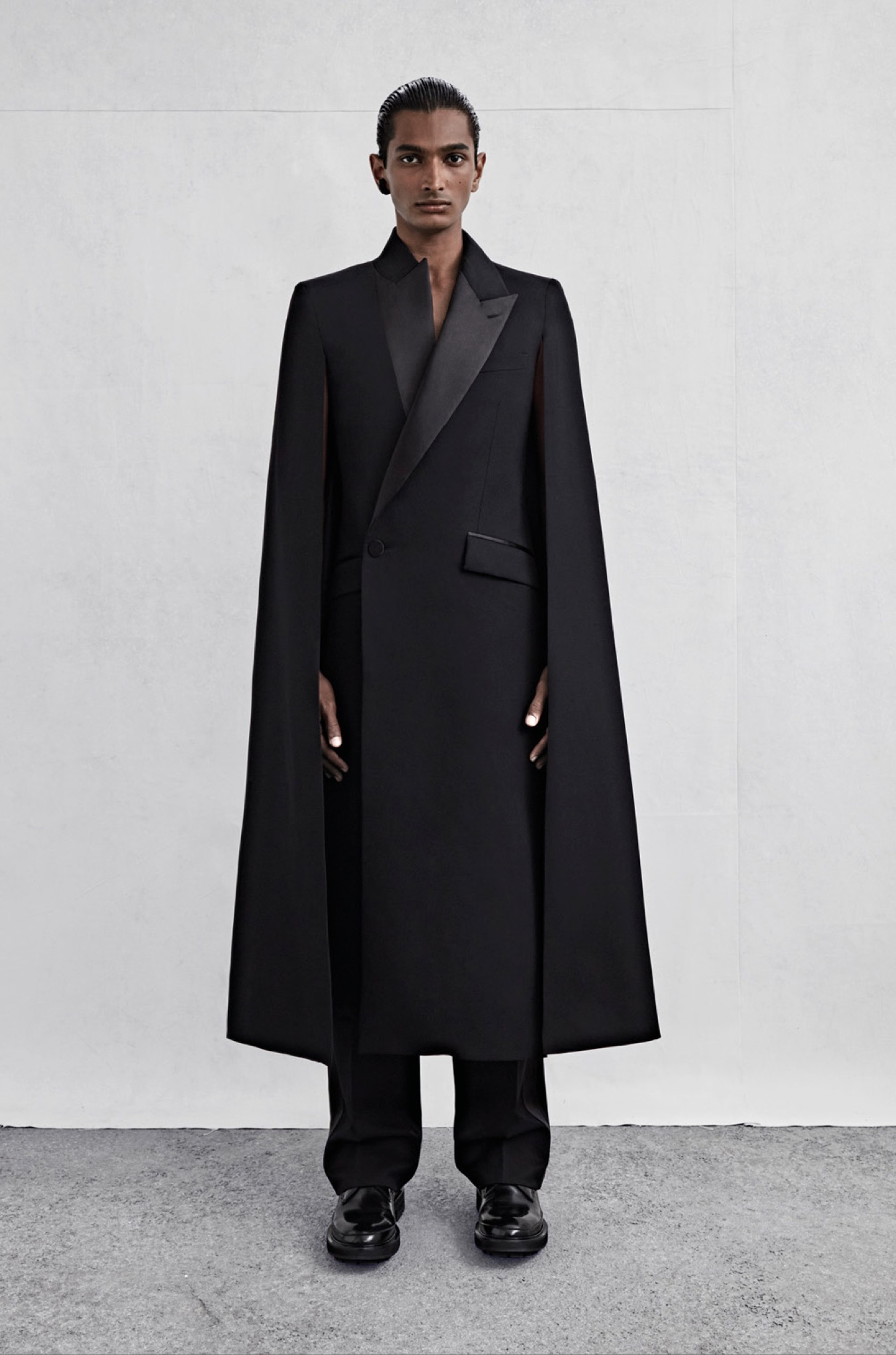 An asymmetric tailored cape coat in black barathea with tonal satin lapels and wide-legged trousers in black barathea with a tonal satin side stripe.
