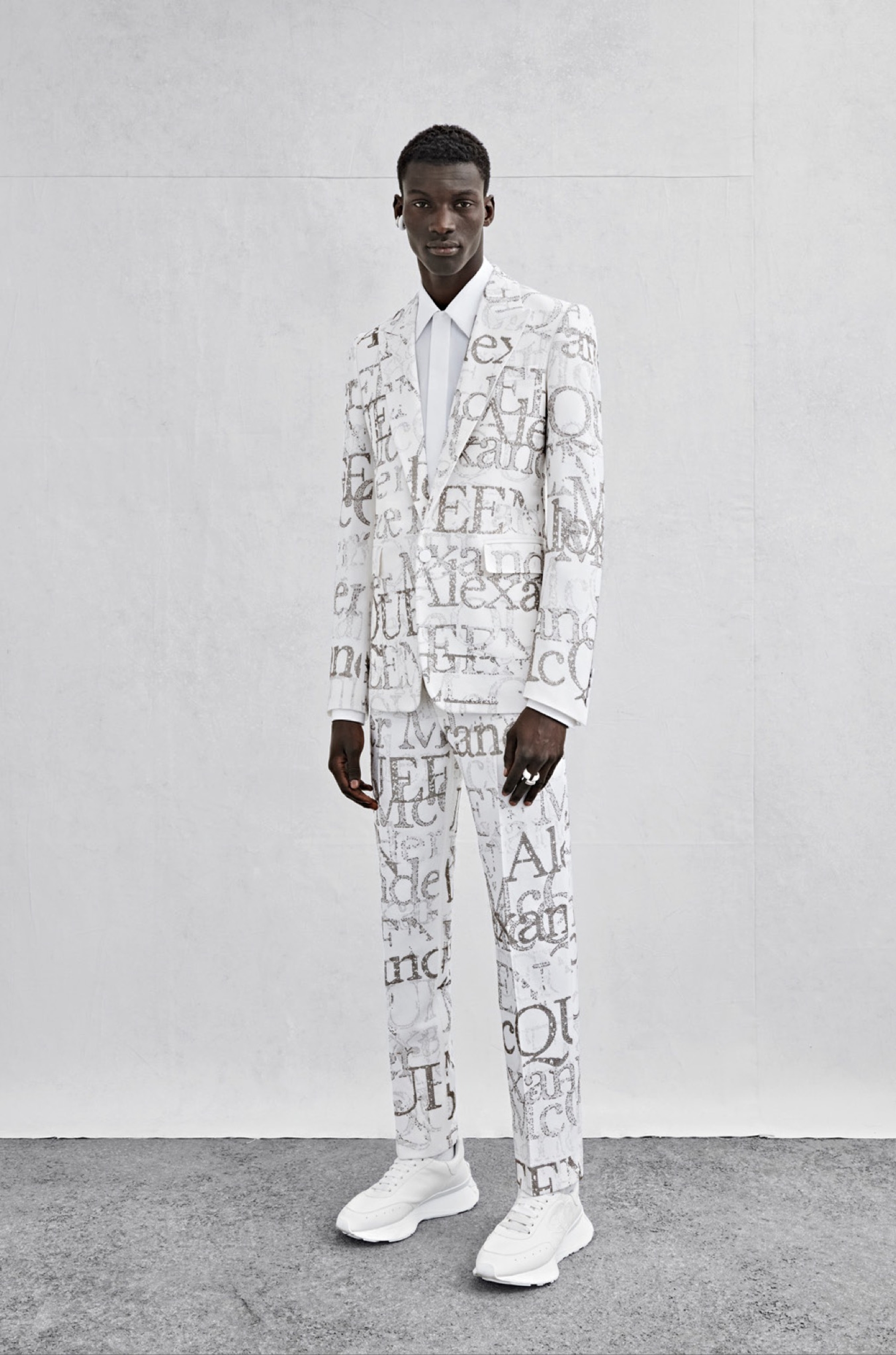 A single-breasted tailored jacket in ivory grain de poudre with metallic sequin logo stamp embroidery, a shirt in white cotton poplin and cigarette trousers in ivory grain de poudre with metallic sequin logo stamp embroidery.