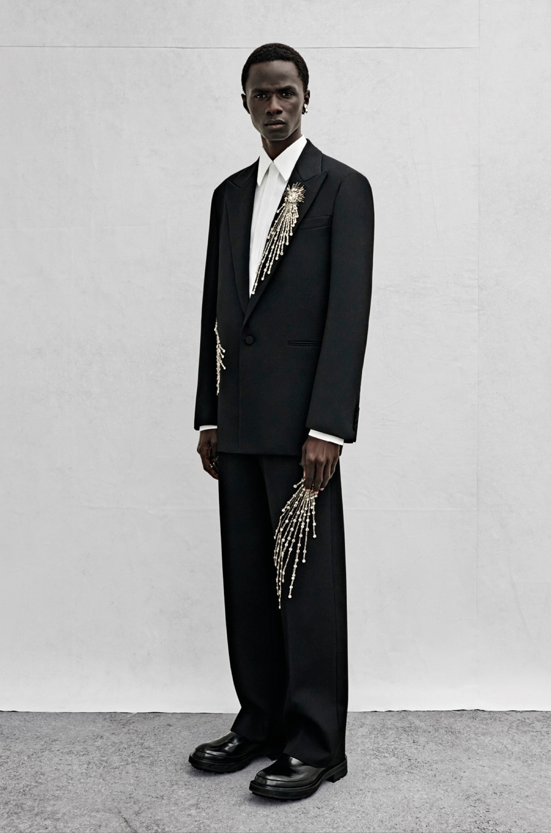 An oversized single-breasted jacket in black wool twill with silver sequin and crystal astral embroidery, a shirt in white cotton poplin and wide-legged trousers in black wool twill with silver sequin and crystal astral embroidery.