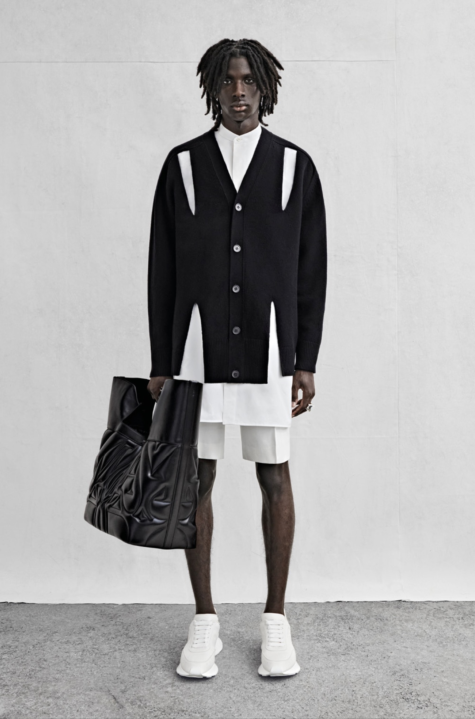 An oversized cardigan with slash detailing in black lambswool, an oversized shirt in white cotton poplin and shorts in white cotton canvas.
