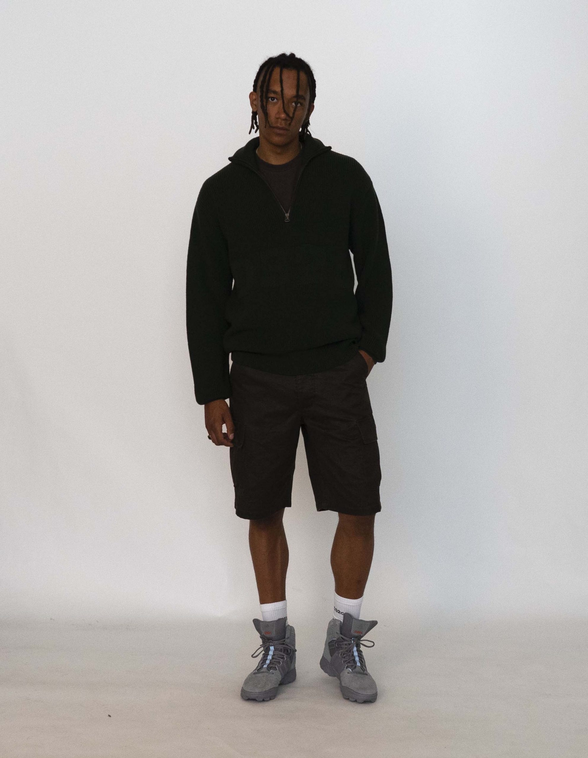 Buyegi wears the 032c LoveSexDreams Knit Troyer in olive and Cargo Shorts with the 032c x adidas Originals GSG-9High Top Sneaker
