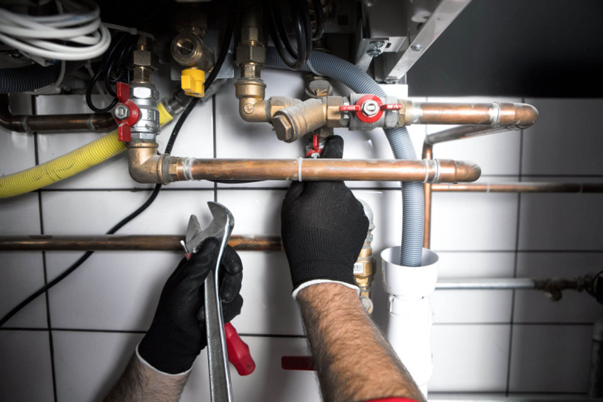 Residential plumber repairing copper water pipes with an adjustable wrench