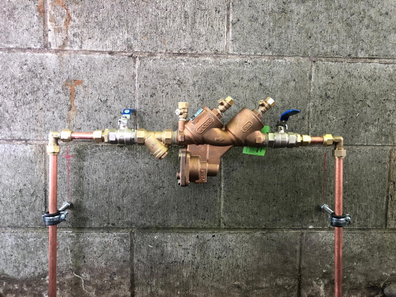 Backflow prevention device connected to copper water pipes against a concrete wall