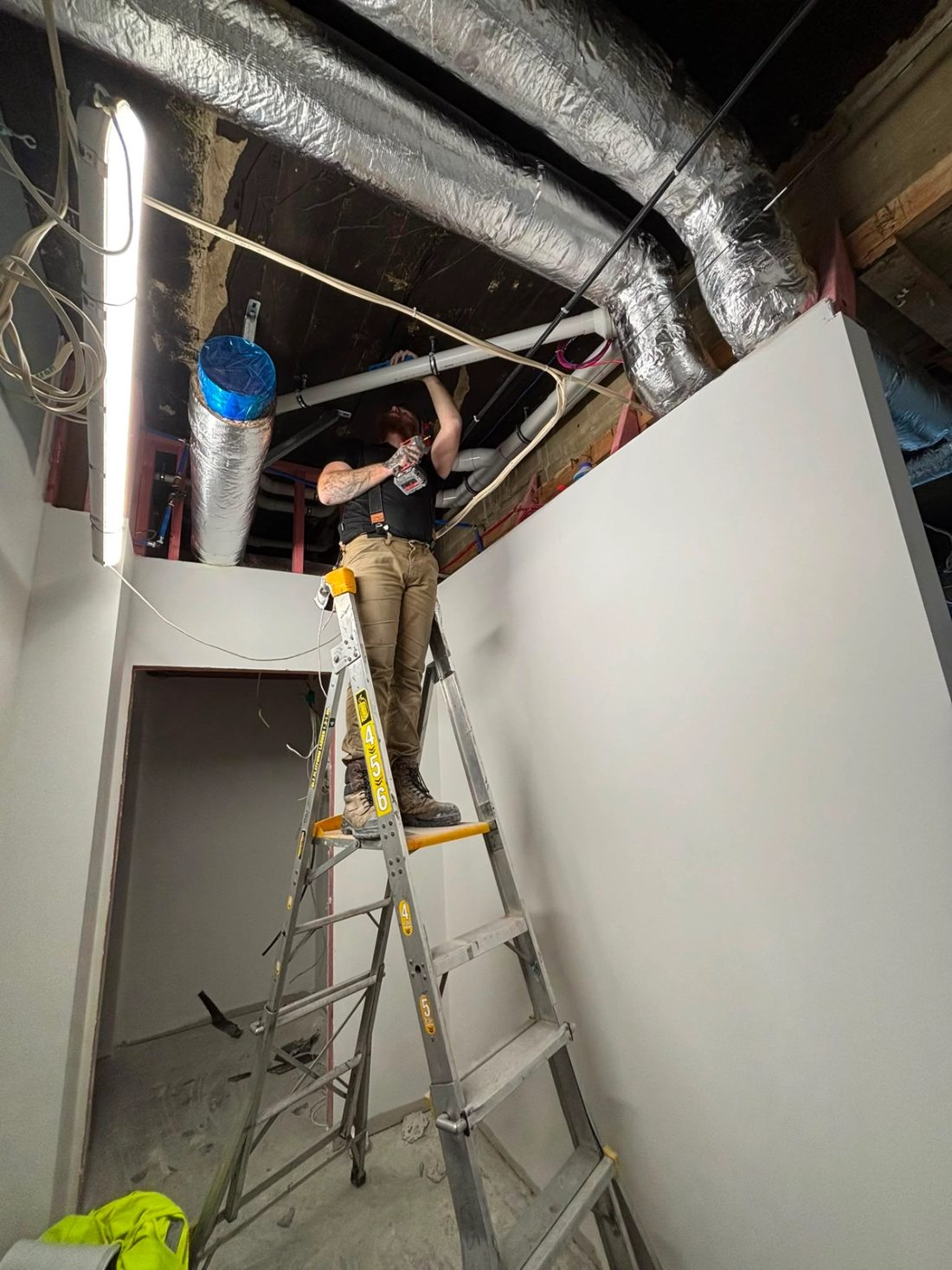 Commercial plumber installing overhead pipework during an interior fit-out