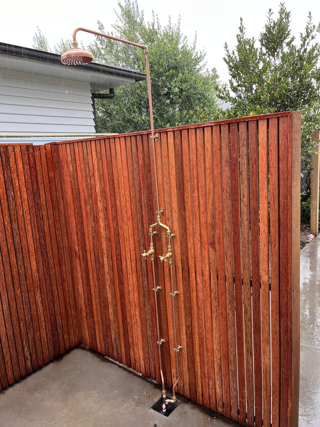Custom copper outdoor shower with brass taps against a timber privacy screen