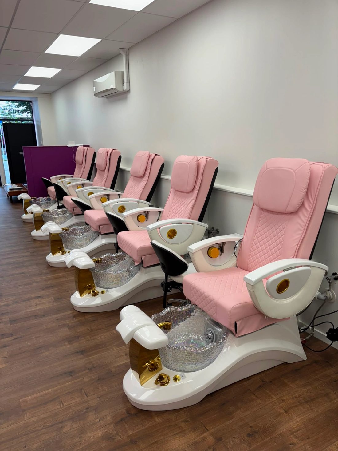 Row of pink pedicure chairs with plumbed foot spa basins in a beauty salon