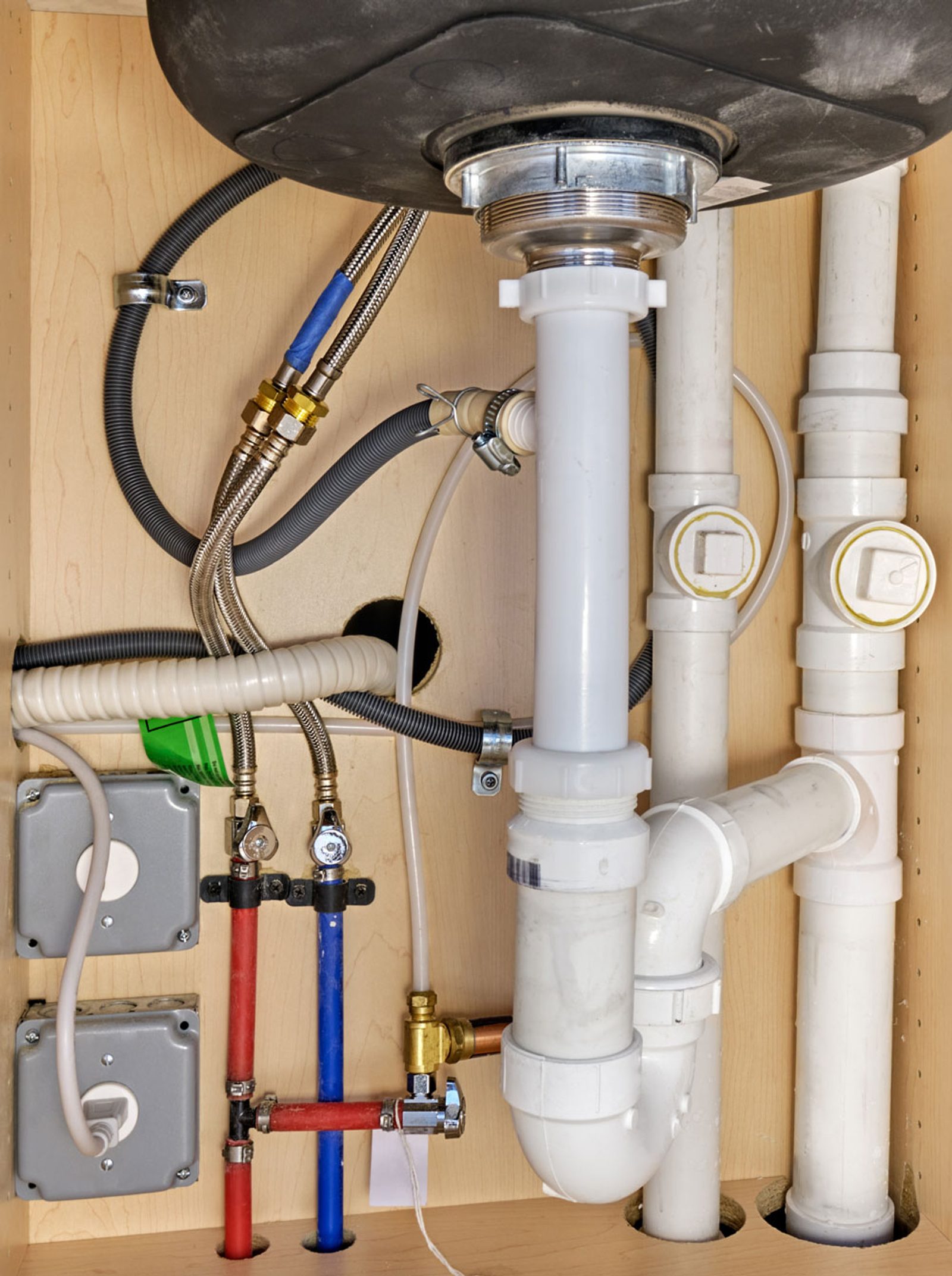 Hot and cold water pipes with drainage plumbing beneath a kitchen sink