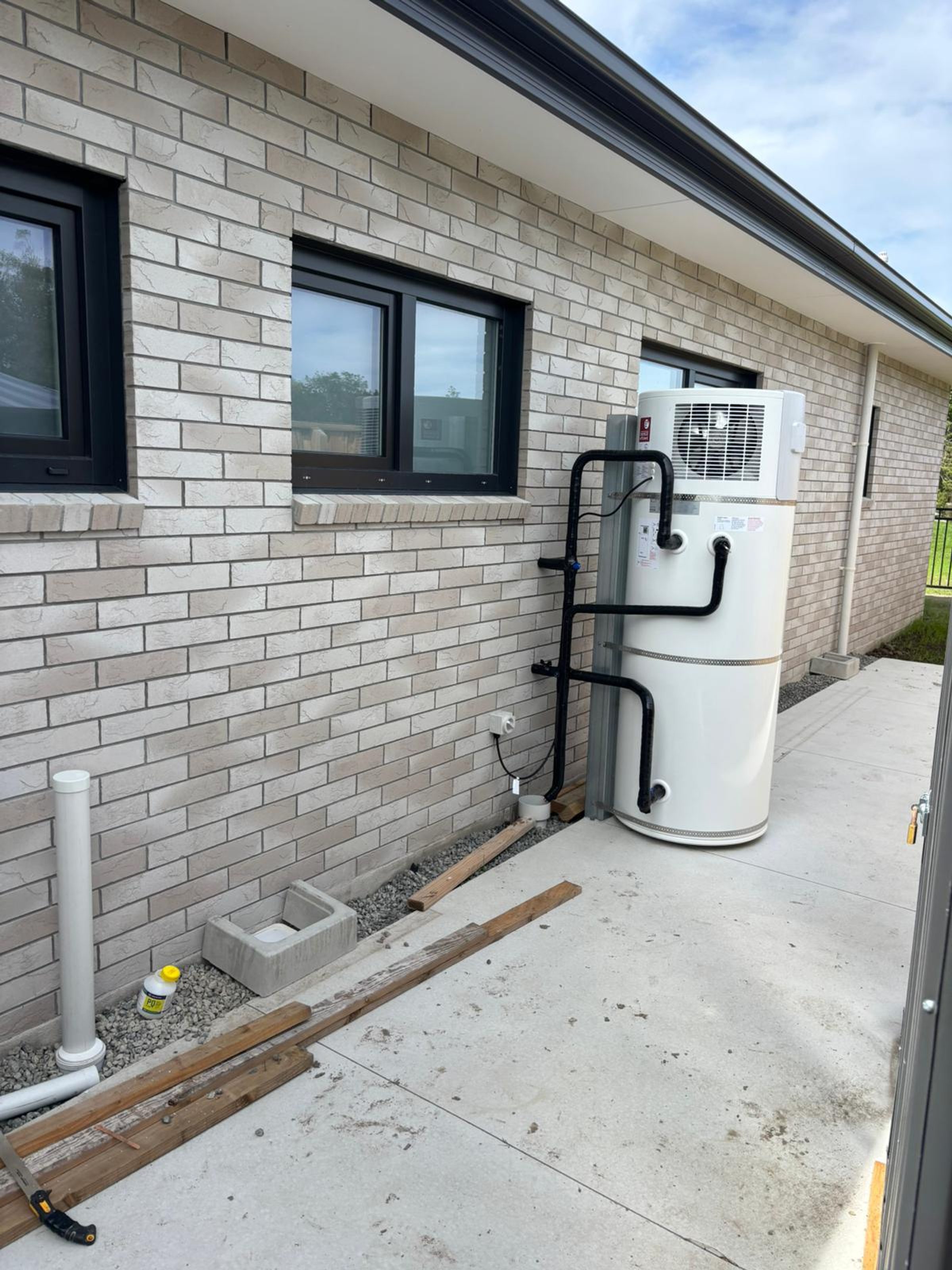 Outdoor heat pump hot water cylinder installed beside a brick home