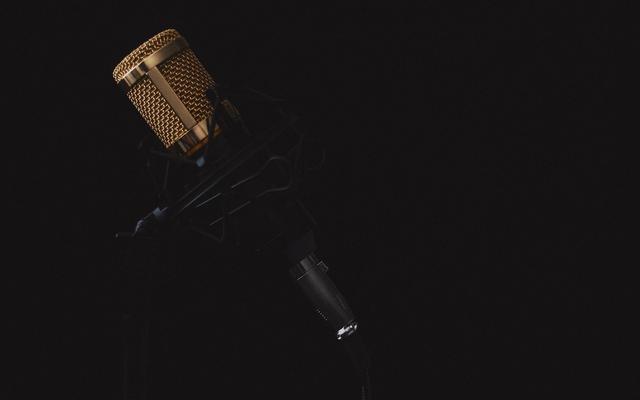 Podcaster merekam podcast menggunakan setup minimal di dalam booth rumahan dengan mikrofon USB dan headphone