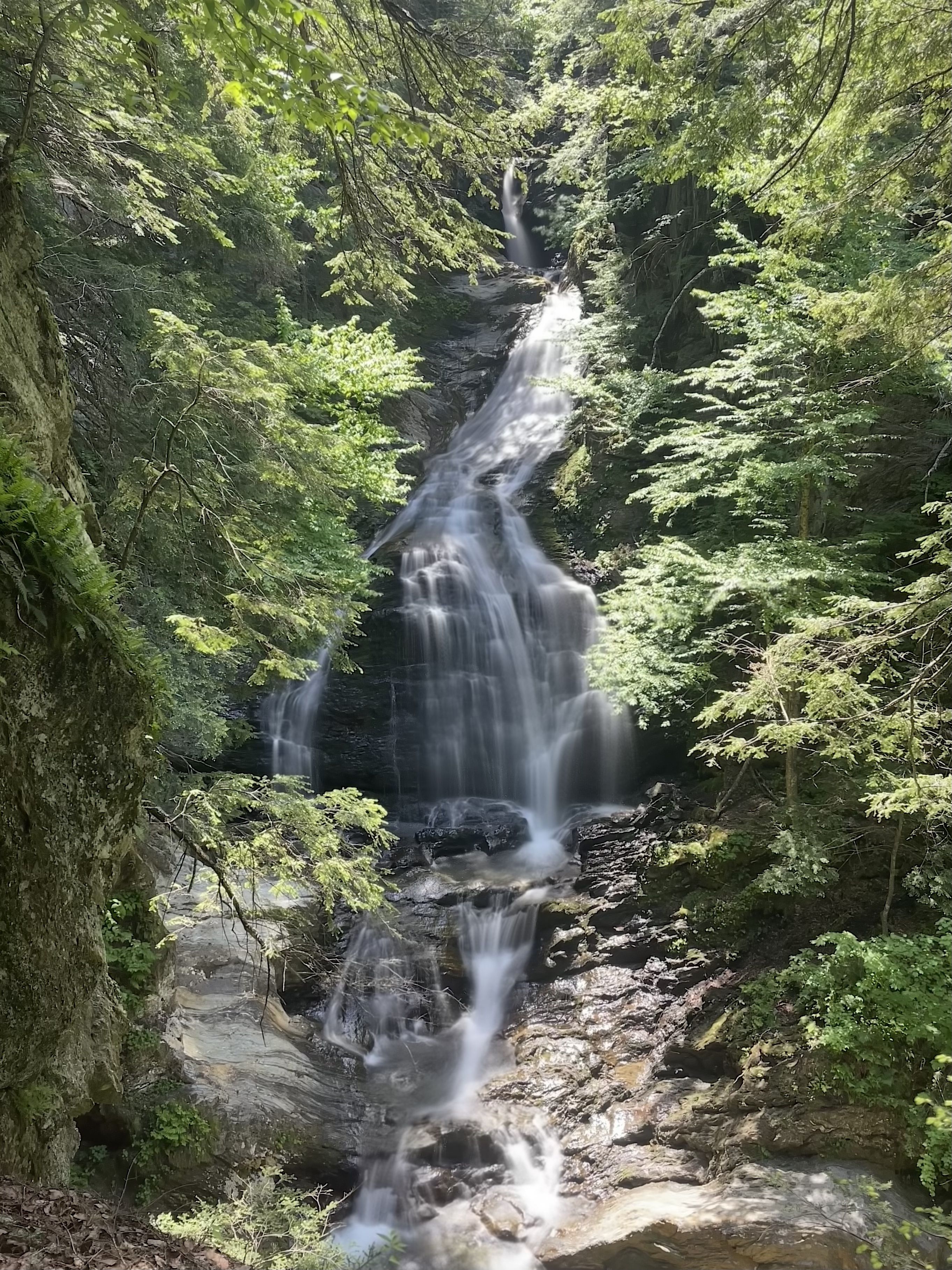 Moss Glen Falls in Stowe, Vermont, cascading over dark rock ledges in a wooded gorge in summer.