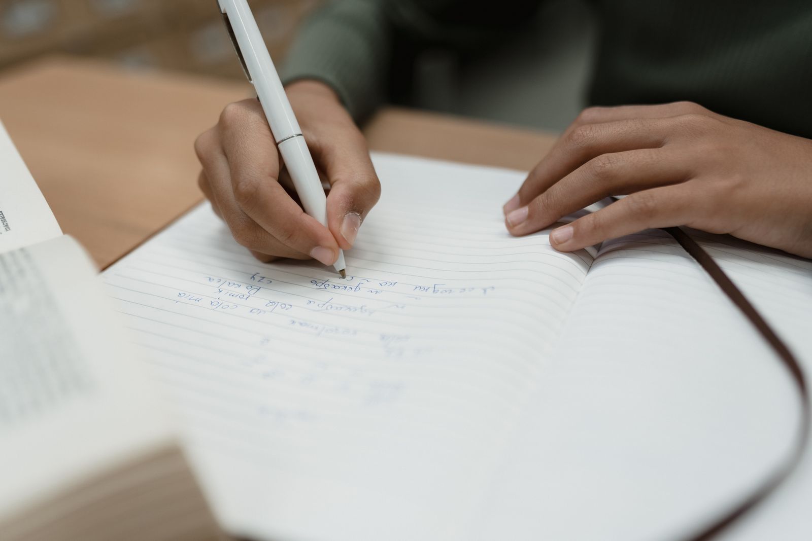 Close-up of a person writing notes in a notebook at a desk