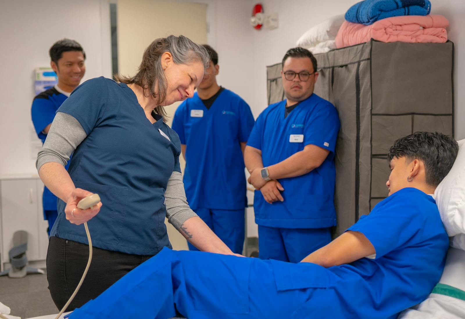 An instructor runs a bedside skills practice with a group of CNA students