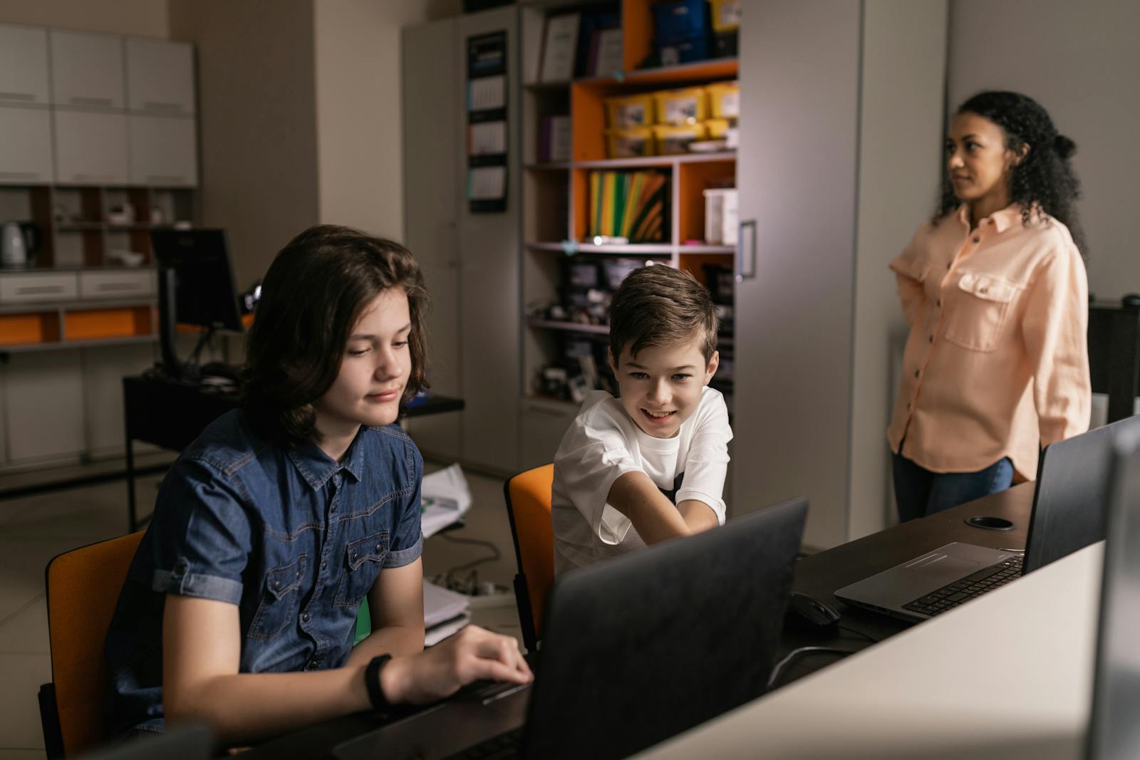 Students working on laptops in a classroom with a teacher guiding them