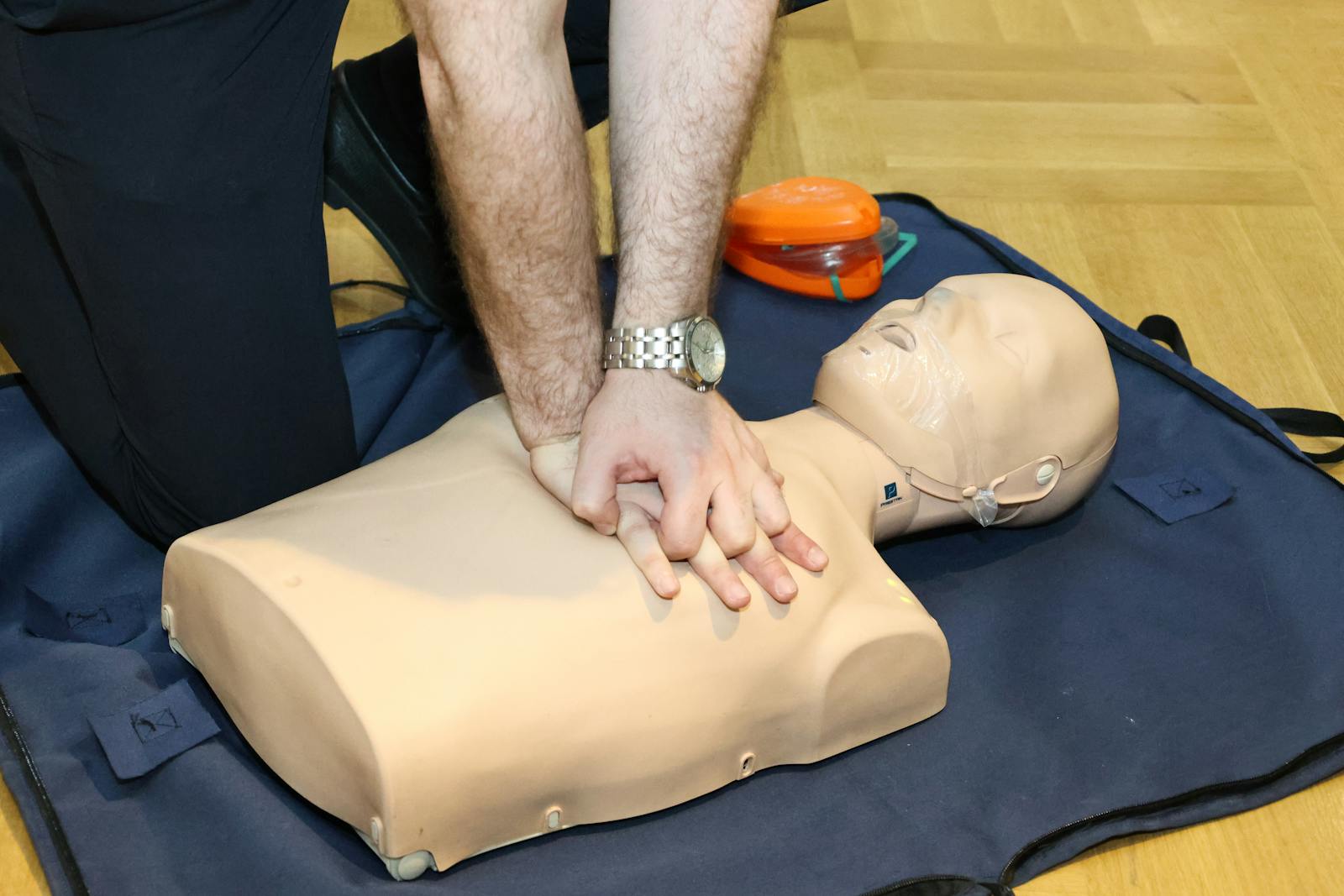 A person practising chest compressions on a CPR training mannequin indoors