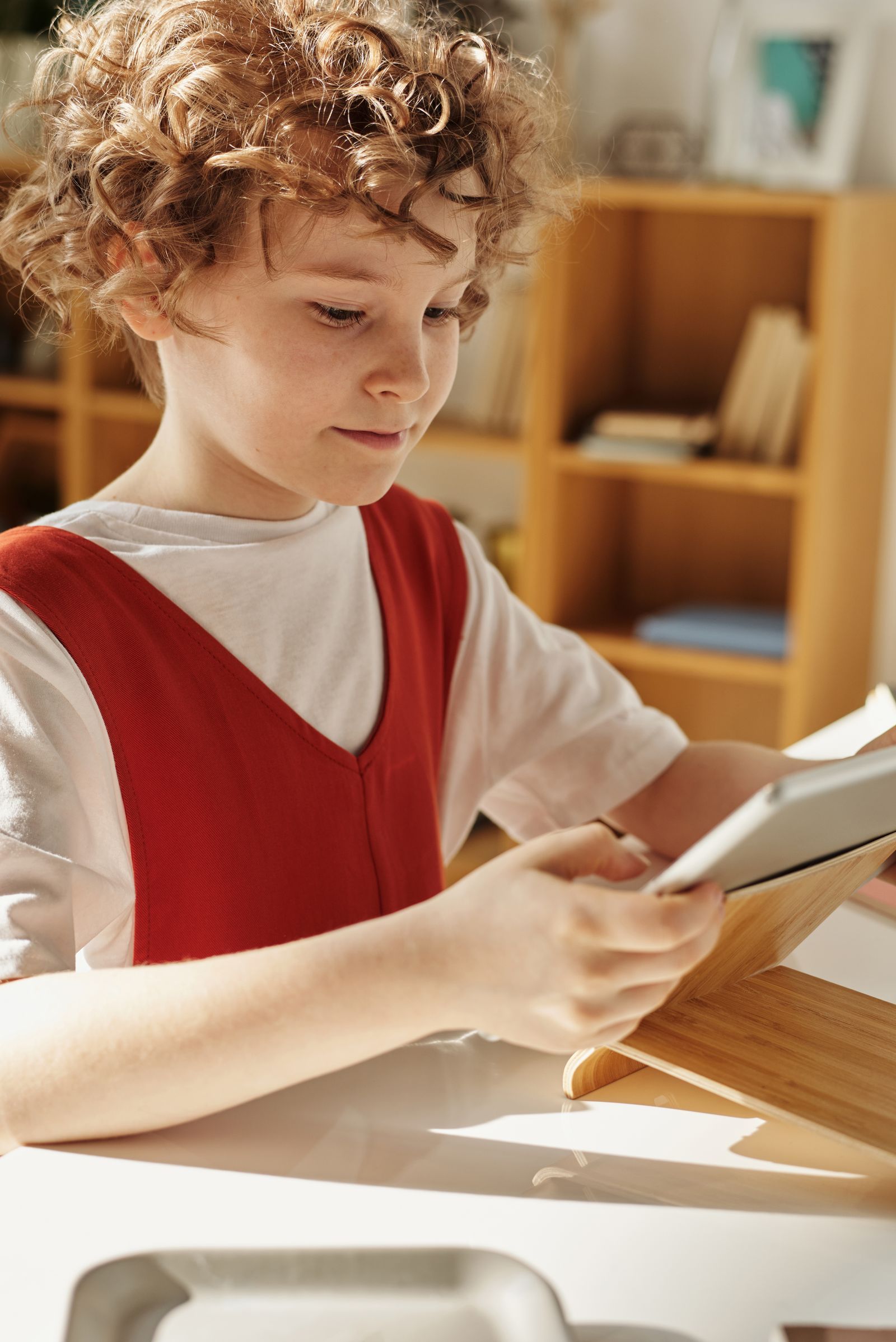 A young child sitting at home using a tablet, focused and at ease