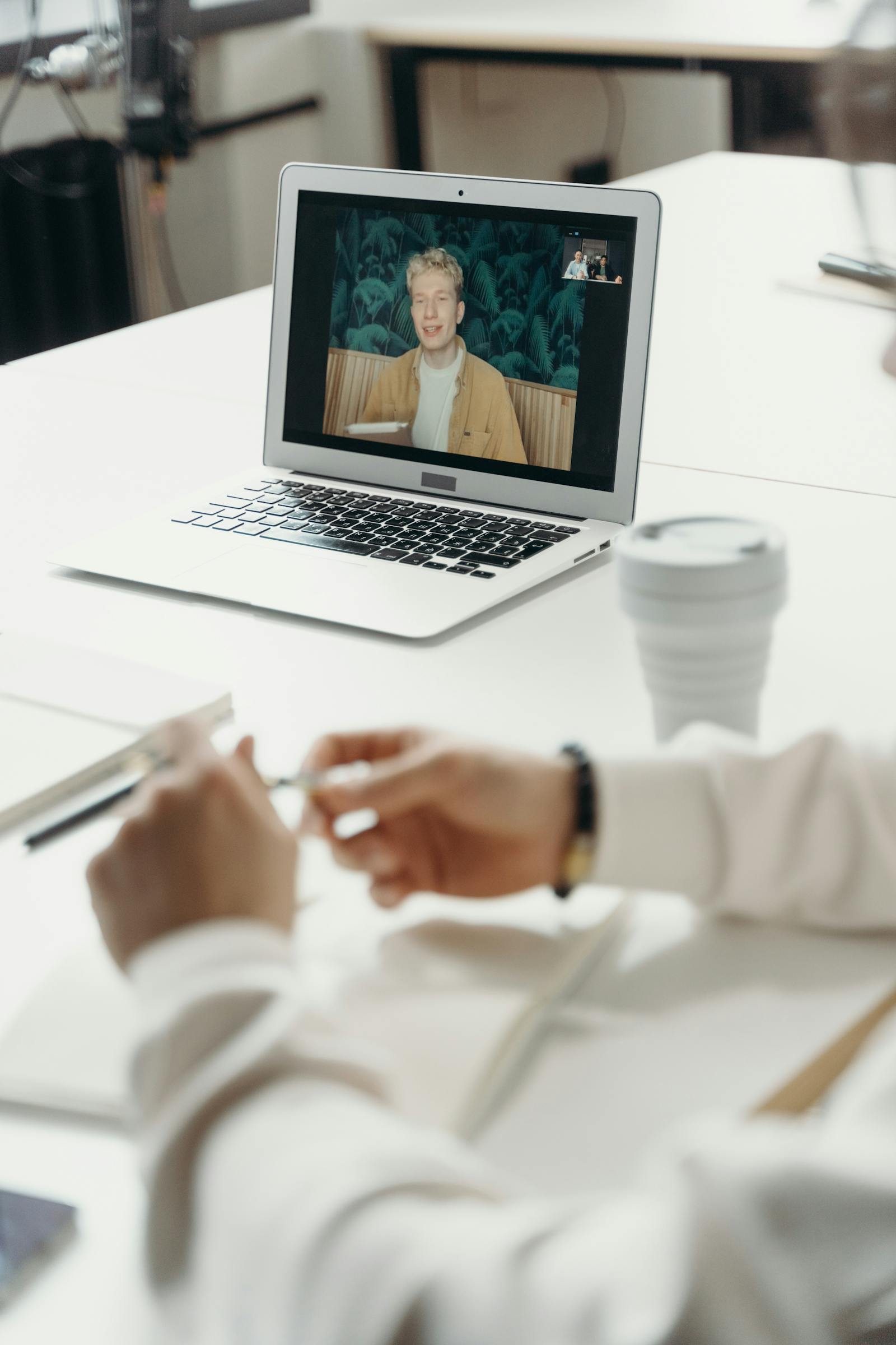 A person on a laptop during a video call with another participant on screen