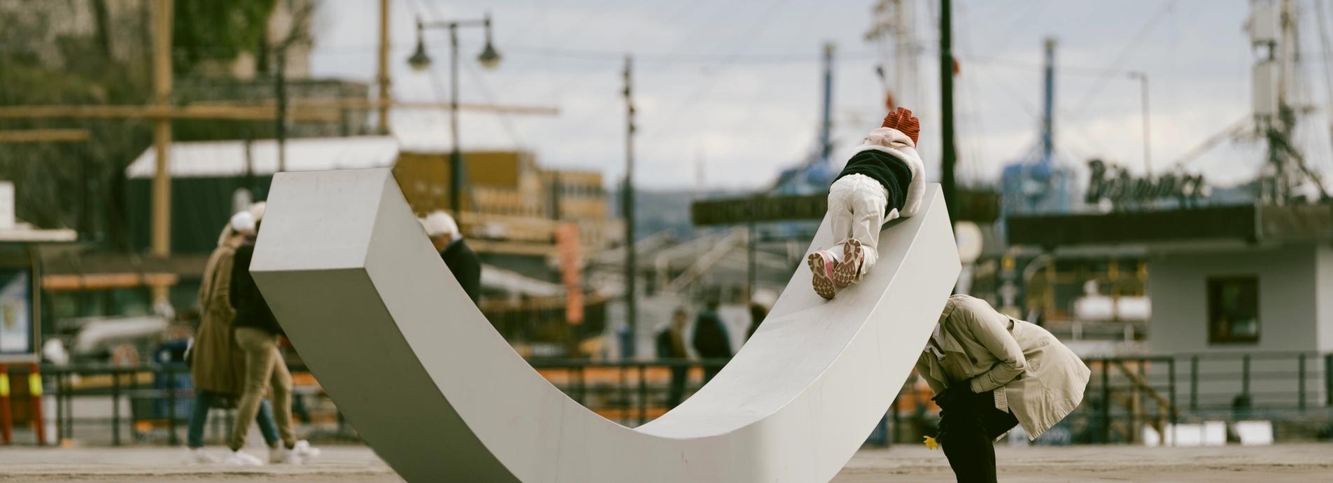 The dialogue bench with a child playing with it, and the mother behind.