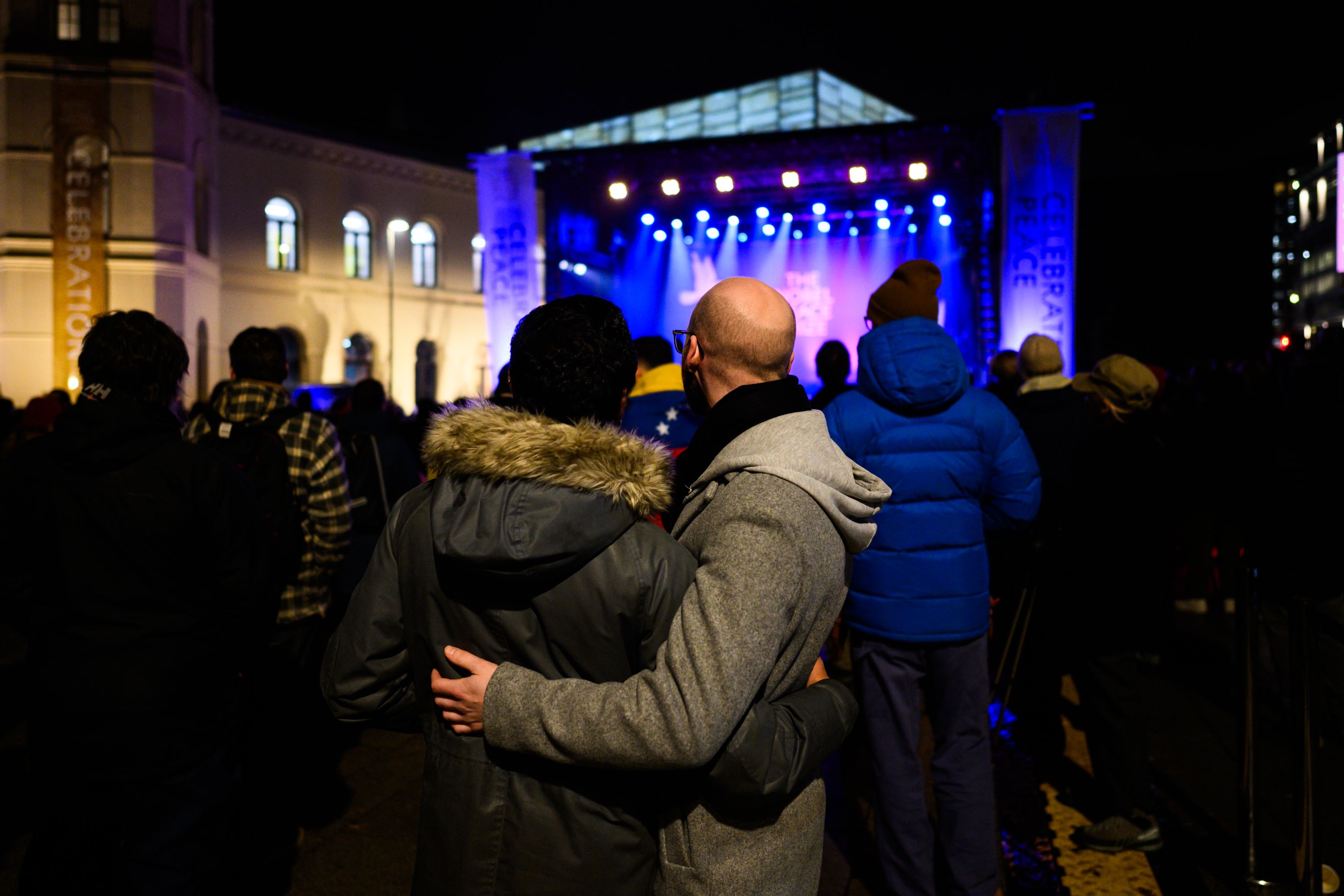 The stage with the crowds in front, two people standing together watching a concert