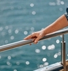 A metal railing, a hand leaning against it, with glittering water in the background.