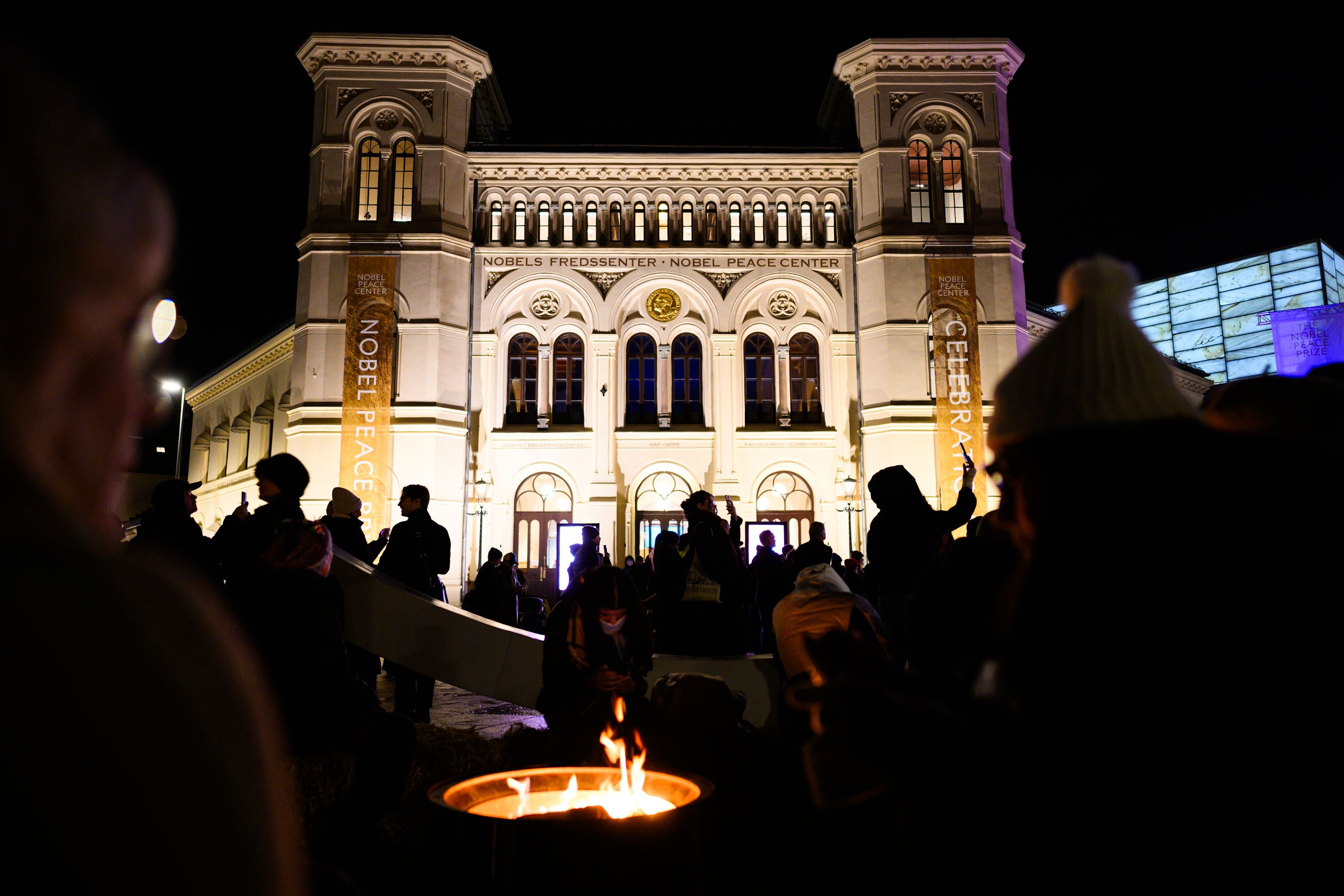 The front of the nobel peace center at nighttime with crowds and a warming fire.
