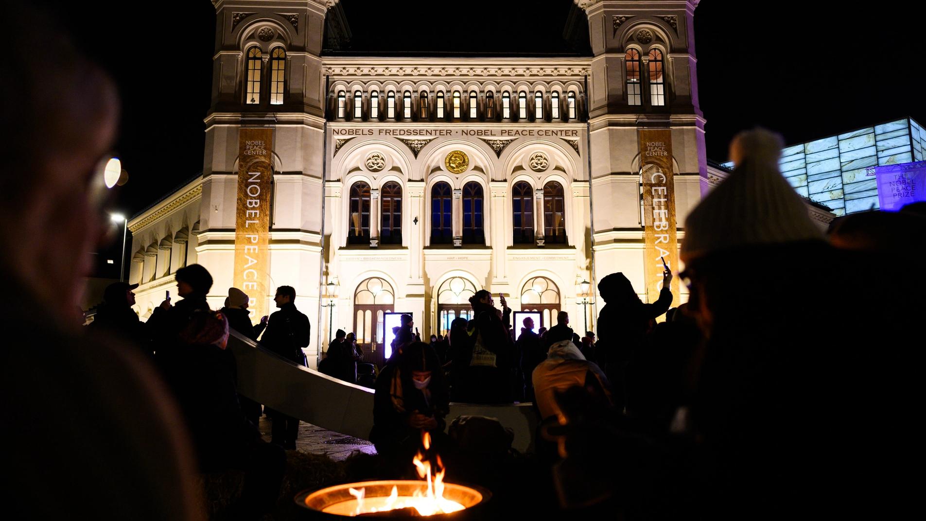 The front of the nobel peace center at nighttime with crowds and a warming fire.