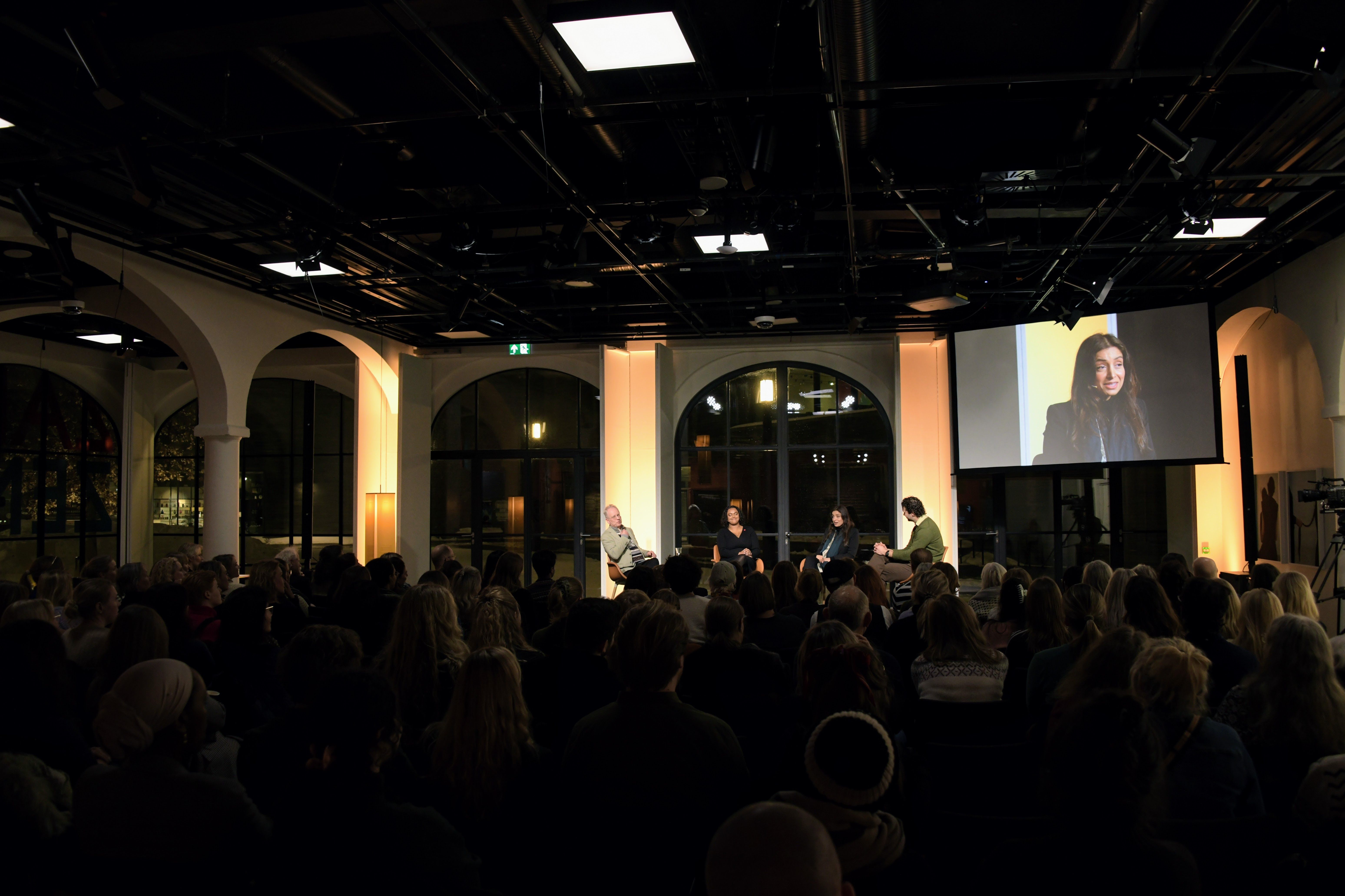 Showing the room called Toghallen, with a big event with several people present. The windows surrounding the stage are big and modern.