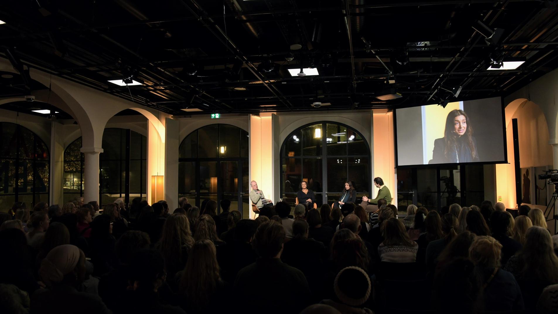 Showing the room called Toghallen, with a big event with several people present. The windows surrounding the stage are big and modern.